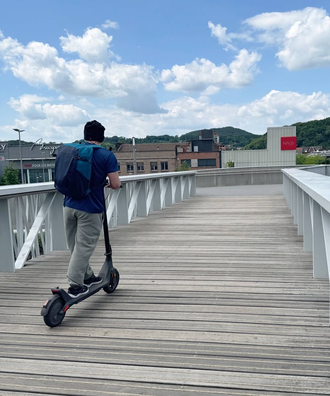 homme à trotinette sur la passerelle des reflets